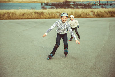 Full length of boy and girl with arms outstretched skating against sky