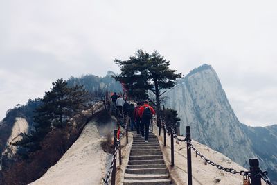 Rear view of people climbing on steps towards mountain against sky
