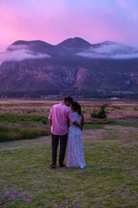 Rear view of woman standing on field against sky during sunset