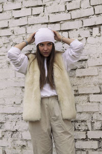 Portrait of woman wearing hat standing against brick wall