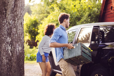 Man holding crate while standing with woman by car on sunny day