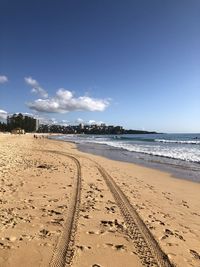 Tire tracks on beach against sky