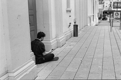 Side view of man sitting on sidewalk in city