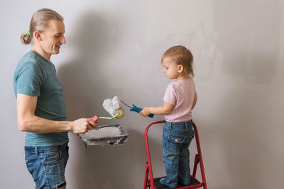 Person holding paint roller over gray wall. father with child paint wall in new house, doing