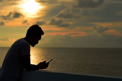 Side view of silhouette man using mobile phone against sunset sky