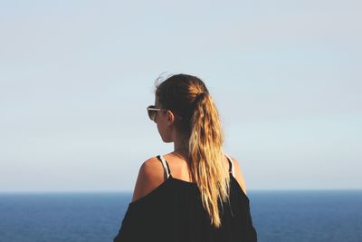 Rear view of woman standing by sea against clear sky