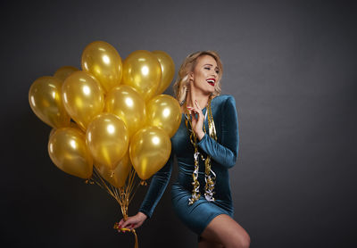 Young woman holding balloons against black background