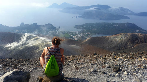 Rear view of woman sitting with bag against mountains and sea