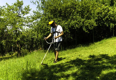 Full length of man cutting grass with weed trimmer