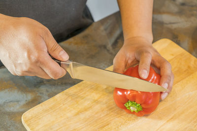 Cropped hands of man chopping red bell pepper on cutting board