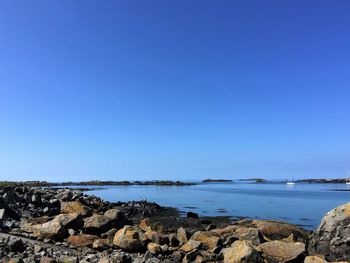 Rocks on shore against clear blue sky