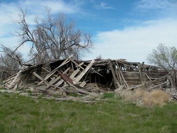 Abandoned house on field against cloudy sky