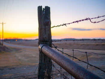 Close-up of barbed wire fence on field against sky during sunset