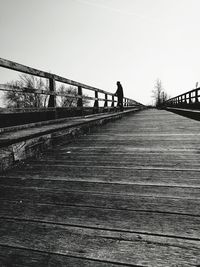 Silhouette man walking on footbridge against clear sky