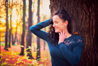 Young woman standing by tree trunk in forest during autumn