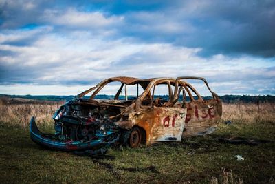 Abandoned car on field against sky