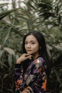 Portrait of young woman standing against plants