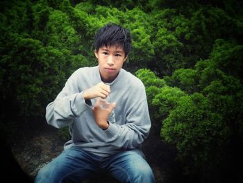 Portrait of boy holding water bottle while sitting against trees