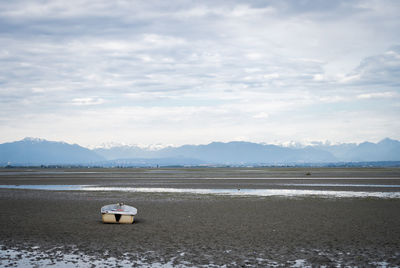 Boat siting on the ground  with cloudy sky and mountains in backdrop, vancouver, bc, canada