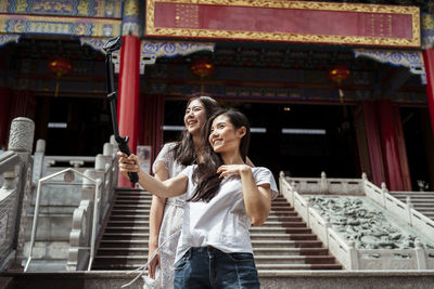 Smiling young woman using smart phone while standing against building