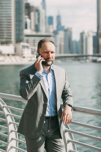 Young businessman with a phone in his hands, standing in a big city among high-rise buildings.