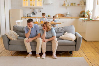 Tense parents sitting on sofa tired crazy loud hyperactive little kids