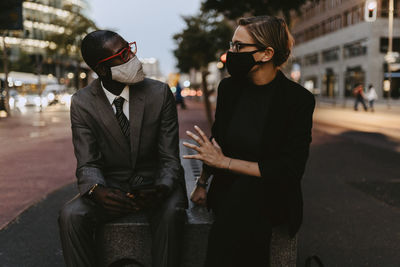 Male and female colleagues discussing on footpath in city during pandemic