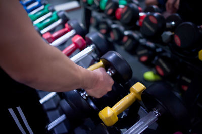 Cropped hand of men lifting dumbbell in gym