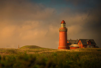 Lighthouse on field against sky during sunset