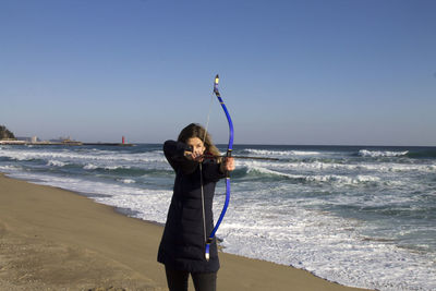 Portrait of young woman standing on beach against clear sky