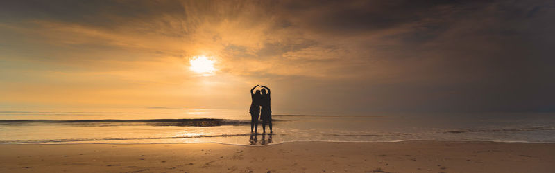 Couple standing on beach against sky during sunset