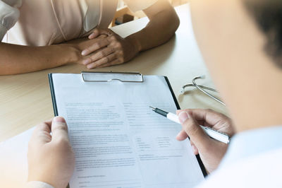 Cropped image of doctor writing prescription while nurse sitting on desk at hospital