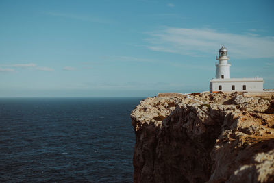 Lighthouse on cliff by sea against sky