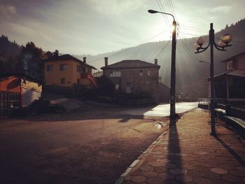 Wet street amidst buildings against sky in city