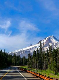 Road amidst trees and snowcapped mountains against sky