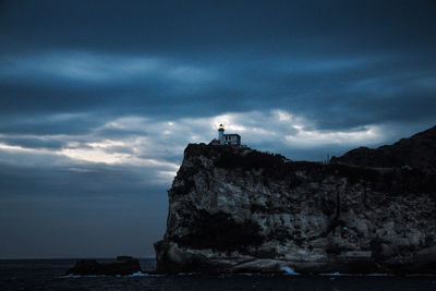 Silhouette of rock formation by sea against sky