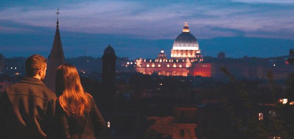 Rear view of people looking at illuminated buildings in city against sky