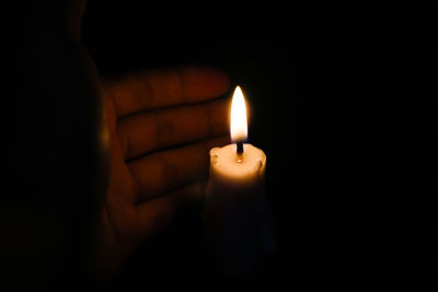 Close-up of hand holding candle in the dark