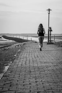 Rear view of woman walking on footpath leading towards beach