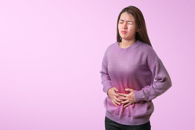 Portrait of young woman standing against pink background