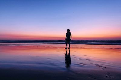 Silhouette man standing on shore against sky during sunset