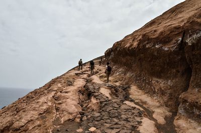 Low angle view of people on rock formation against sky