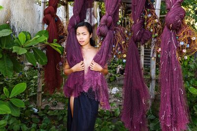 Portrait of shirtless woman holding purple fishing nets while standing by plants