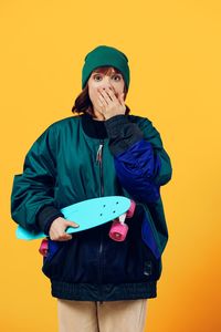 Young woman standing against yellow background