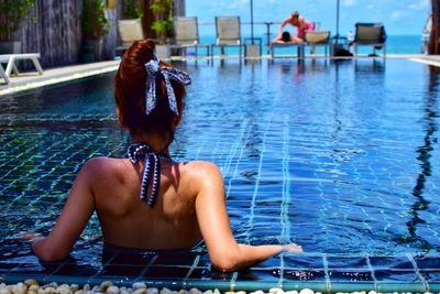 Rear view of shirtless woman sitting in swimming pool