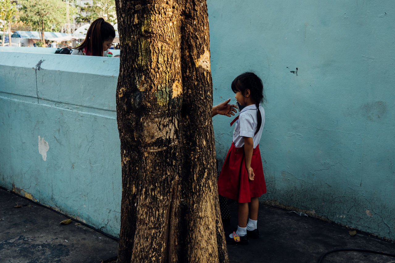 women, full length, casual clothing, real people, child, girls, standing, wall - building feature, childhood, day, females, tree trunk, lifestyles, trunk, people, leisure activity, two people, emotion, outdoors, hairstyle, innocence, teenager, contemplation