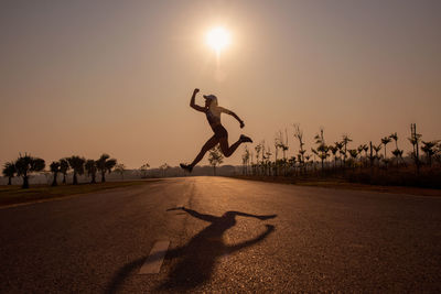 Silhouette woman jumping on road against sky during sunset