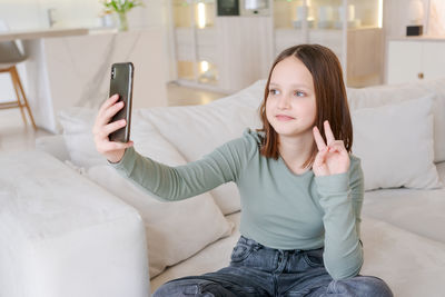  girl is sitting on couch and taking picture  herself with her cell phone. she is smiling and happy