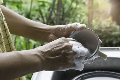 Cropped hands of man cleaning utensils in sink