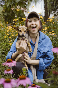 Portrait of happy young woman with terrier dog kneeling amidst flowers in park